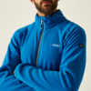 Mann mit Bart trägt eine blaue Jacke mit Reißverschluss, vor hellem Hintergrund
