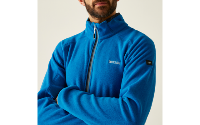 Mann mit Bart trägt eine blaue Jacke mit Reißverschluss, vor hellem Hintergrund