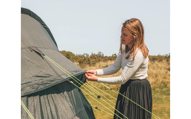 Frau spannt Zeltleine an einem grünen Zelt im Freien