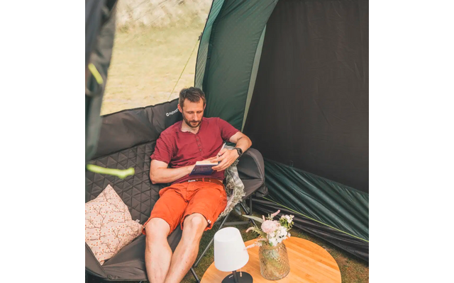 Mann sitzt auf einem Sessel im Zelt und liest ein Buch, neben ihm ein Tisch mit Vase und Lampe