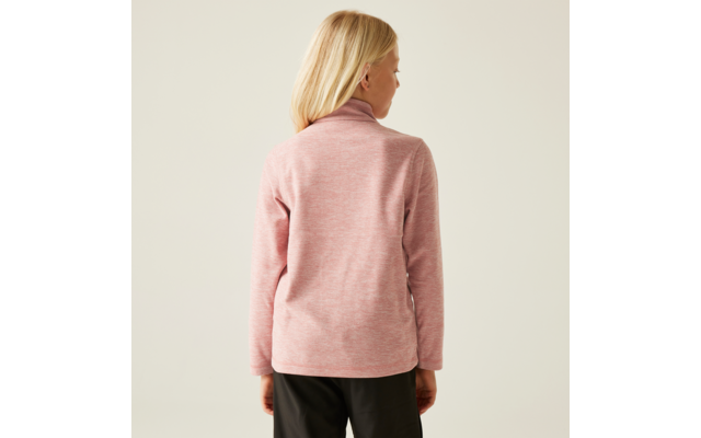 Vue de dos d'une personne aux cheveux blonds mi-longs, portant un pull à col roulé rose et un pantalon sombre sur fond clair