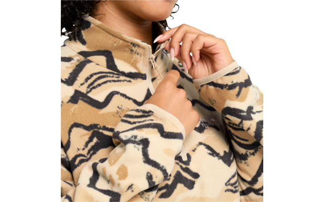 Nahaufnahme einer Person, die mit beiden Händen den Reißverschluss einer beige gemusterten Fleecejacke hochzieht; Kinn und Hals sichtbar