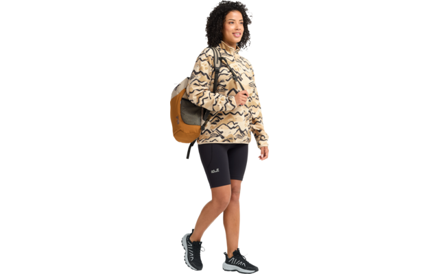 Person geht nach rechts, trägt beige-schwarz gemusterten Kapuzenpullover, schwarze Radshorts, schwarze Sportschuhe, senffarbenen Rucksack und hat dunkle, lockige Haare
