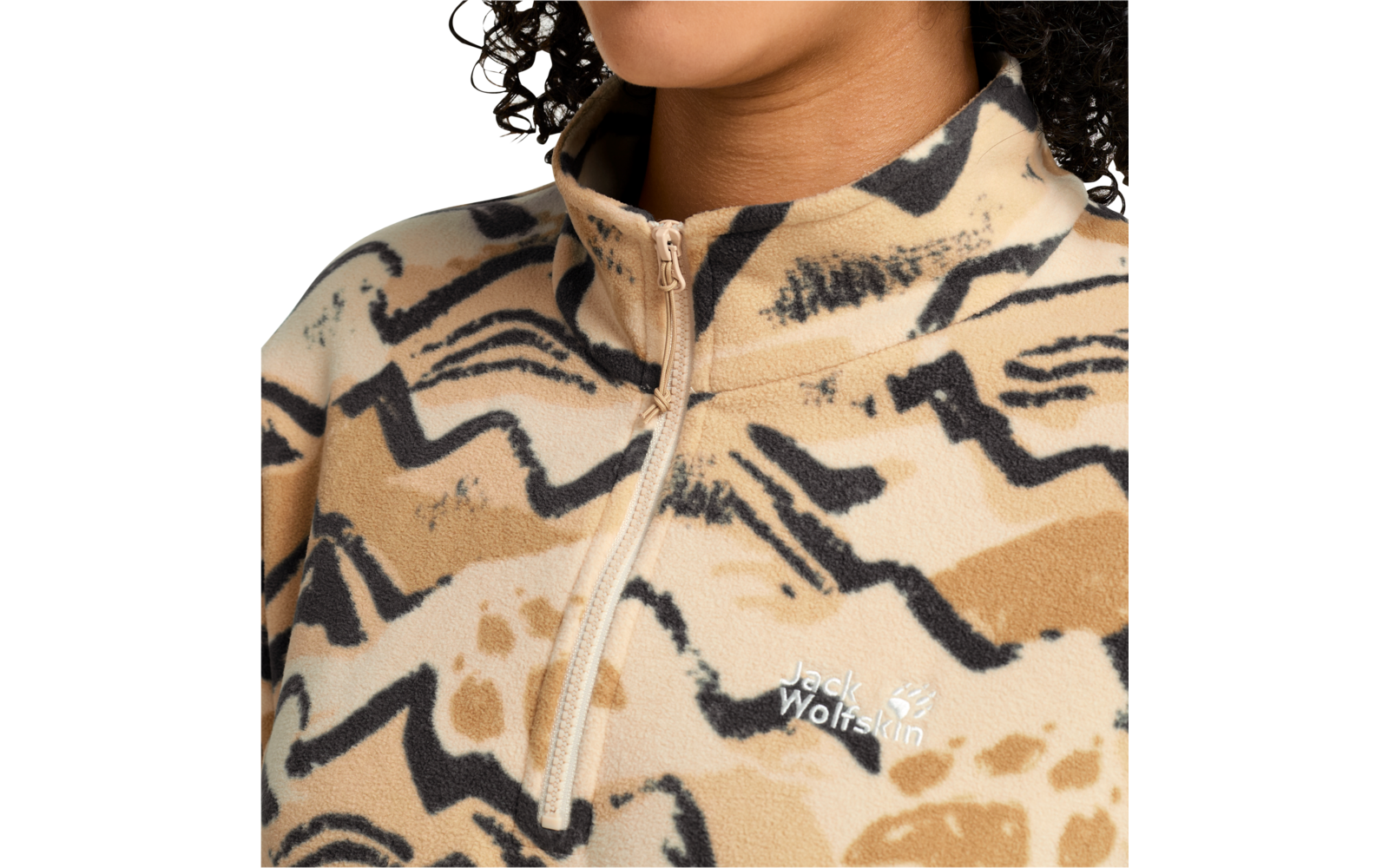 Nahaufnahme von Kinn, Hals und Schultern; beiger Fleecepullover mit abstraktem schwarz-braunem Muster, kurzer Reißverschluss vorn und gesticktes "Jack Wolfskin"-Logo