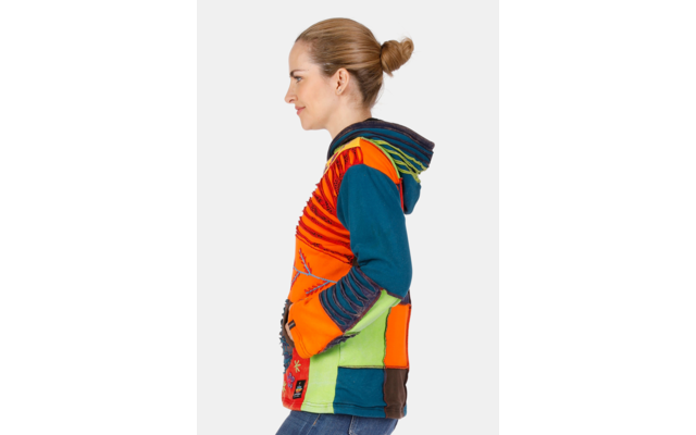 Seitliche Aufnahme einer Person mit hochgestecktem Haar, die eine bunte Patchwork-Kapuzenjacke und Jeans trägt vor weißem Hintergrund