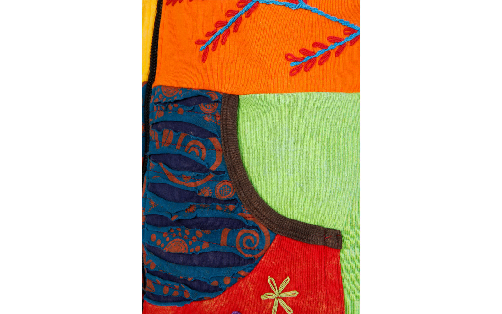 Nahaufnahme eines bunten Stoffpatchworks mit orangefarbenen, grünen und roten Flächen, einer blau gemusterten Tasche mit braunem Rand und gestickten Blumen- und Blattmotiven