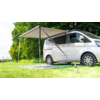 White camper van with an extended awning on a grassy area next to trees