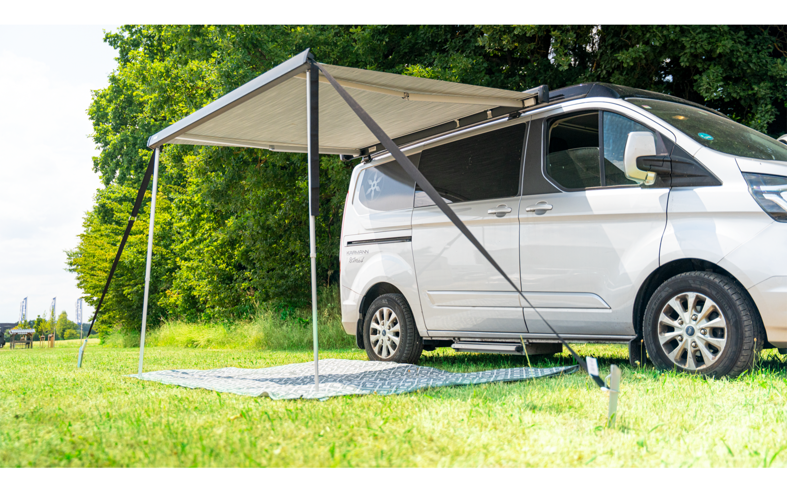 White camper van with an extended awning on a grassy area next to trees