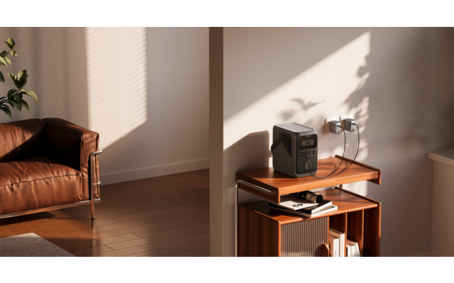 Braunes Ledersofa links, Zimmerpflanze, hölzernes Beistellregal mit tragbarem Radio oben und Büchern, Steckdose an der Wand, Sonnenlicht und Schatten auf Wand und Parkettboden