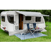 Witte caravan met open deur en twee blauwe campingstoelen naast een klaptafel met borden en bekers op een blauw grondzeil