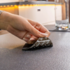 Main aux ongles manucurés décollant un autocollant noir avec texte blanc d'un plateau de table texturé ; verre sur un dessous de verre en arrière-plan