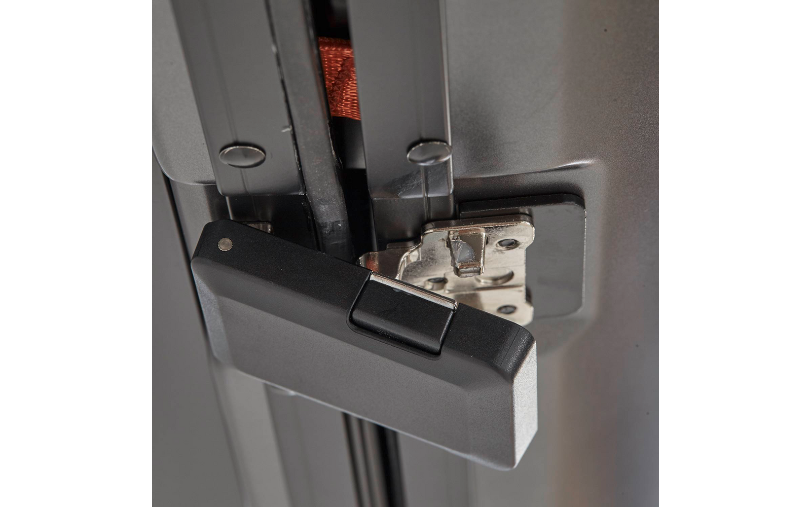 Schwarzer rechteckiger Griff mit Drucktaste, befestigt an einem grauen Metallrahmen und einer silbernen Metallplatte mit Schrauben; im Spalt ein orangenes Band sichtbar