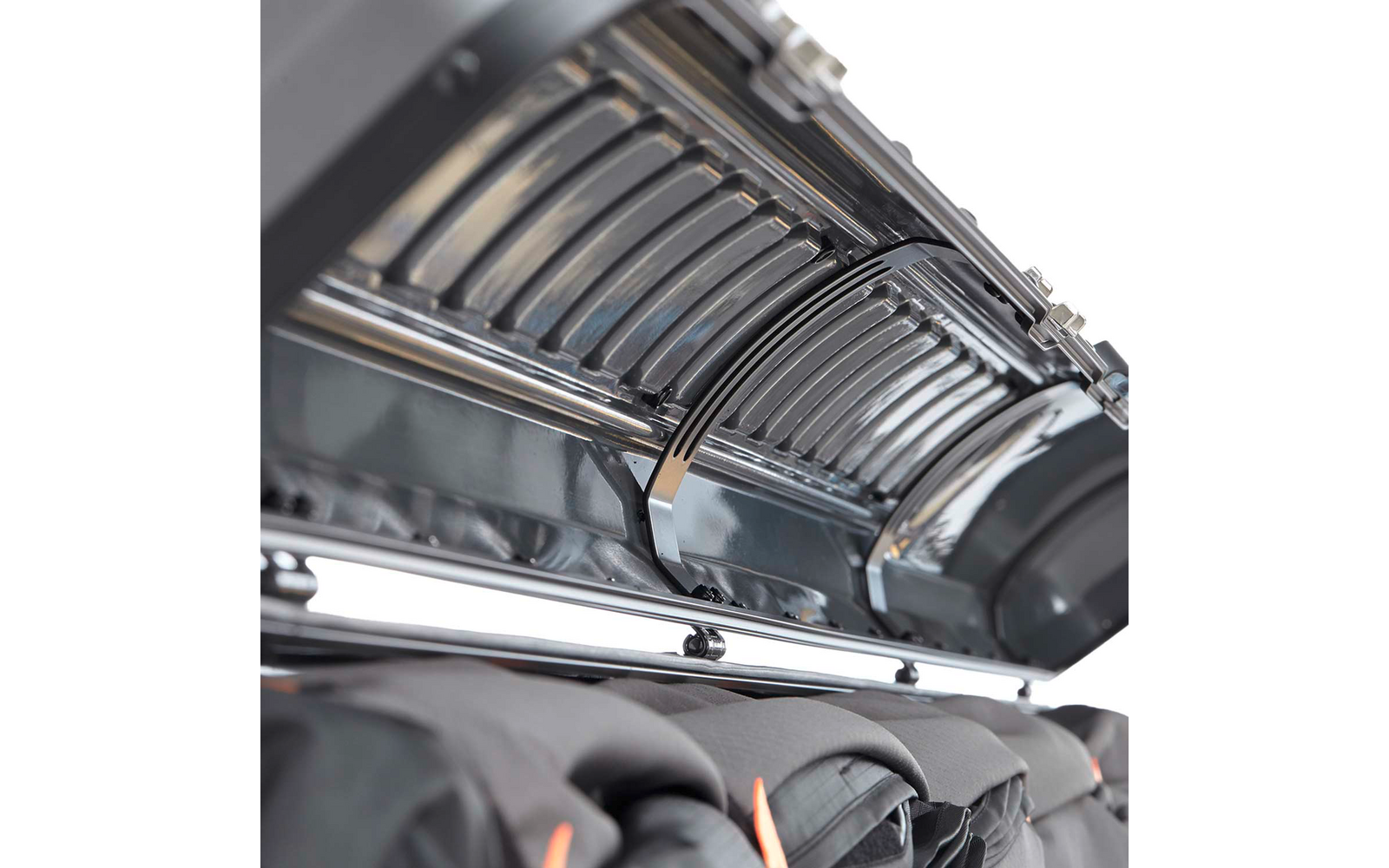 Nahaufnahme eines geöffneten metallischen Gehäuses mit gebogenen Lamellen und glänzenden Metallstäben, darunter schwarze Jacken mit orangefarbenen Details