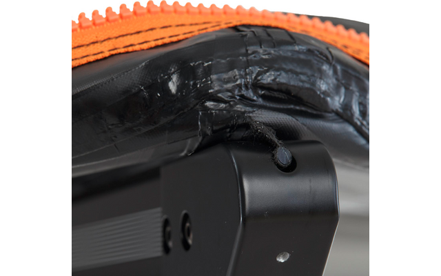 Nahaufnahme eines schwarzen Polsters mit orangefarbener, gezackter Kante, überlappendem schwarzen Klebeband mit abstehenden Fasern und einem angrenzenden schwarzen Kunststoffteil mit zwei Schrauben und rundem Loch