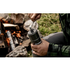 Hands of a person turning the crank of a cylindrical hand grinder, a campfire on grass in the background
