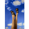 Dos piernas levantadas con sandalias negras frente a un cielo azul con nubes blancas