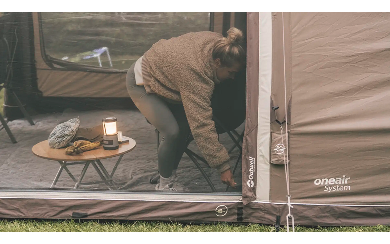 Person hält eine wasserdichte Schüssel neben einem Campingzelt, auf dem Boden steht ein kleiner Campingtisch mit Utensilien