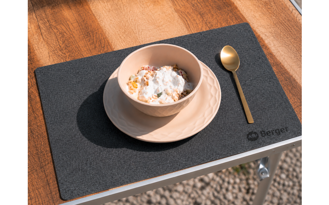 Helle Schale mit flockigen Stücken und heller Creme auf Unterteller, goldfarbener Löffel rechts, schwarzer rechteckiger Tischuntersetzer auf Holzoberfläche, Teil eines Metalltisches sichtbar