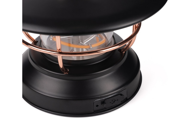 Zwarte ronde metalen voet met USB‑aansluiting, koperkleurige metalen stangen, heldere glazen lamp met zichtbaar gloeidraad, zwarte kaprand