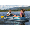 Zwei Personen sitzen in einem aufblasbaren Boot auf einem See, mit Schwimmwesten; Berge und teilweise bewölkter Himmel im Hintergrund