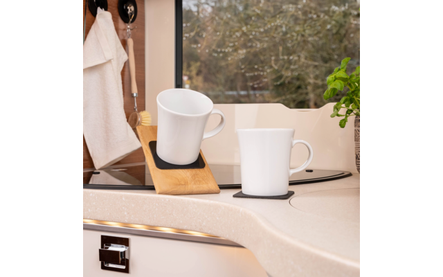Two white mugs on a kitchen countertop, one on a wooden holder, window with trees in the background