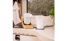 Zwei weiße Tassen auf einem Küchenarbeitsplatte, eine auf einem Holzhalter, im Hintergrund Fenster mit Blick auf Bäume