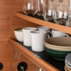 Open kitchen cabinet with white mugs, bowls, and glasses