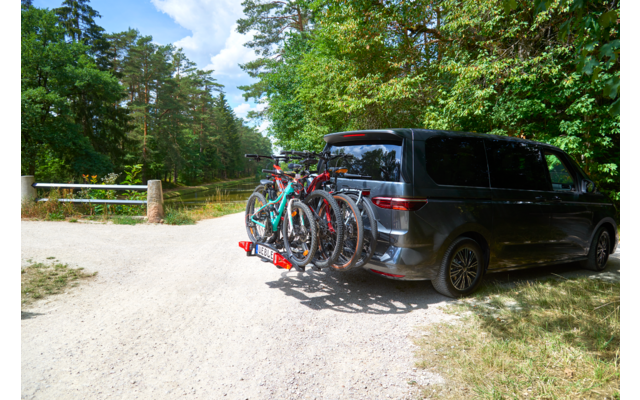 Donkere minivan op een grindpad naast bomen, vier fietsen op een achterdrager