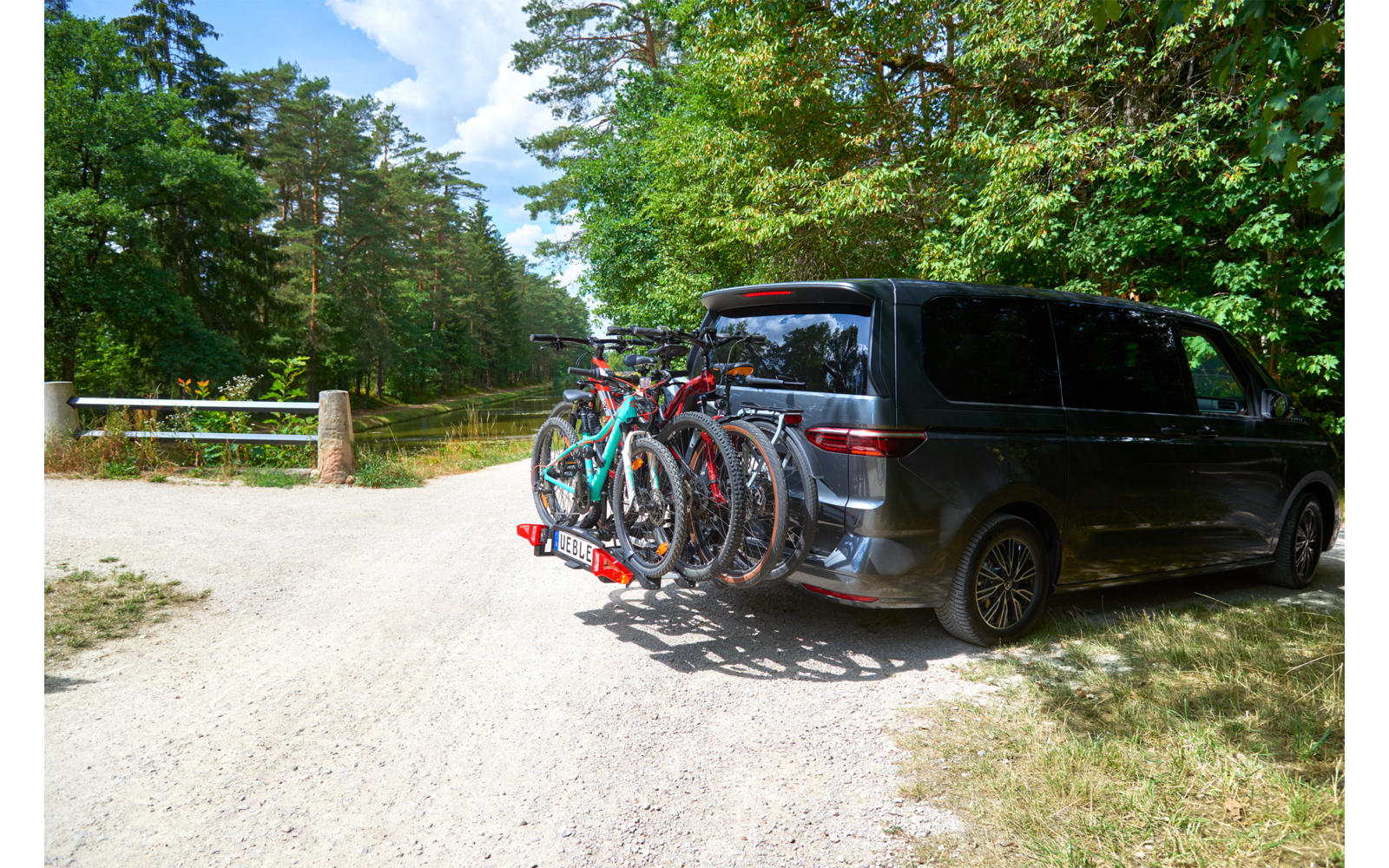 Donkere minivan op een grindpad naast bomen, vier fietsen op een achterdrager