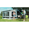 Motorhome with attached awning on a meadow, a table with camping chairs in front of the awning, a woman and a man are outside