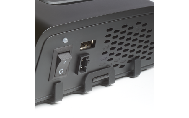 Nahaufnahme der Rückseite eines schwarzen Geräts mit Kippschalter (I/O), kleiner runder Leuchte, USB-A-Anschluss, rechteckigem Anschluss, wabenförmigem Belüftungsgitter und zwei Kunststoffhaltern