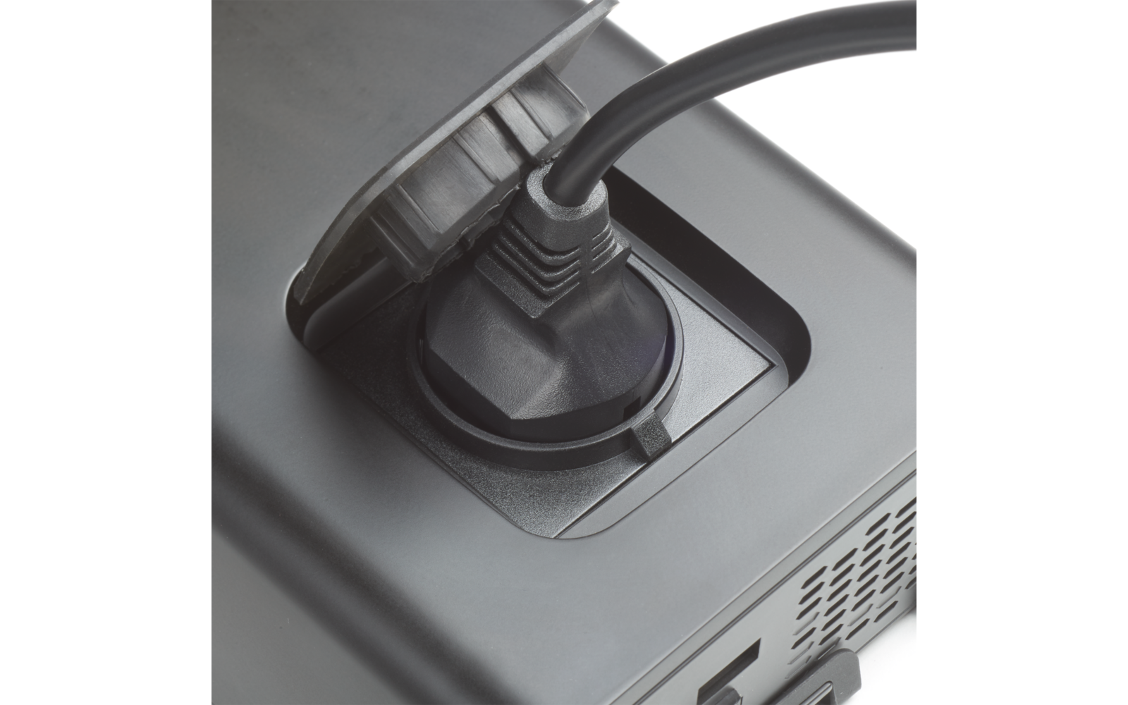 Schwarzer Netzstecker in rundem Anschluss eines grauen elektronischen Geräts, Lüftungsgitter sichtbar