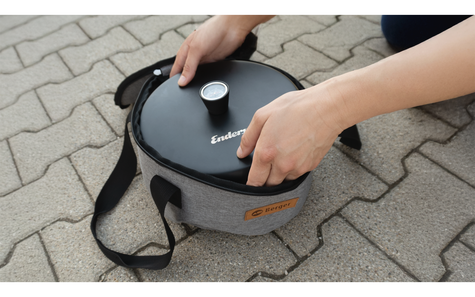 Des mains soulèvent un conteneur isolé gris avec un couvercle noir et un thermomètre sur un trottoir