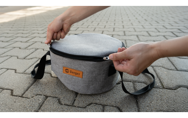 Des mains ouvrent une pochette ronde grise sur un sol pavé