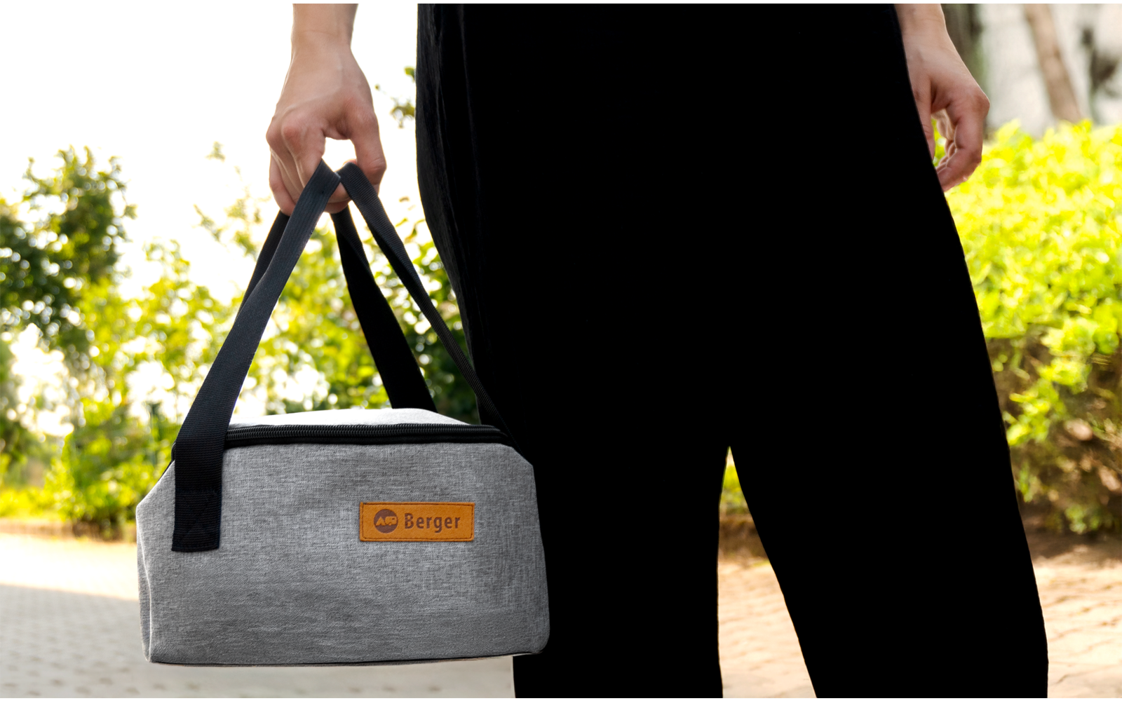 Person hält eine graue Kühltasche mit schwarzem Tragegriff und Lederetikett