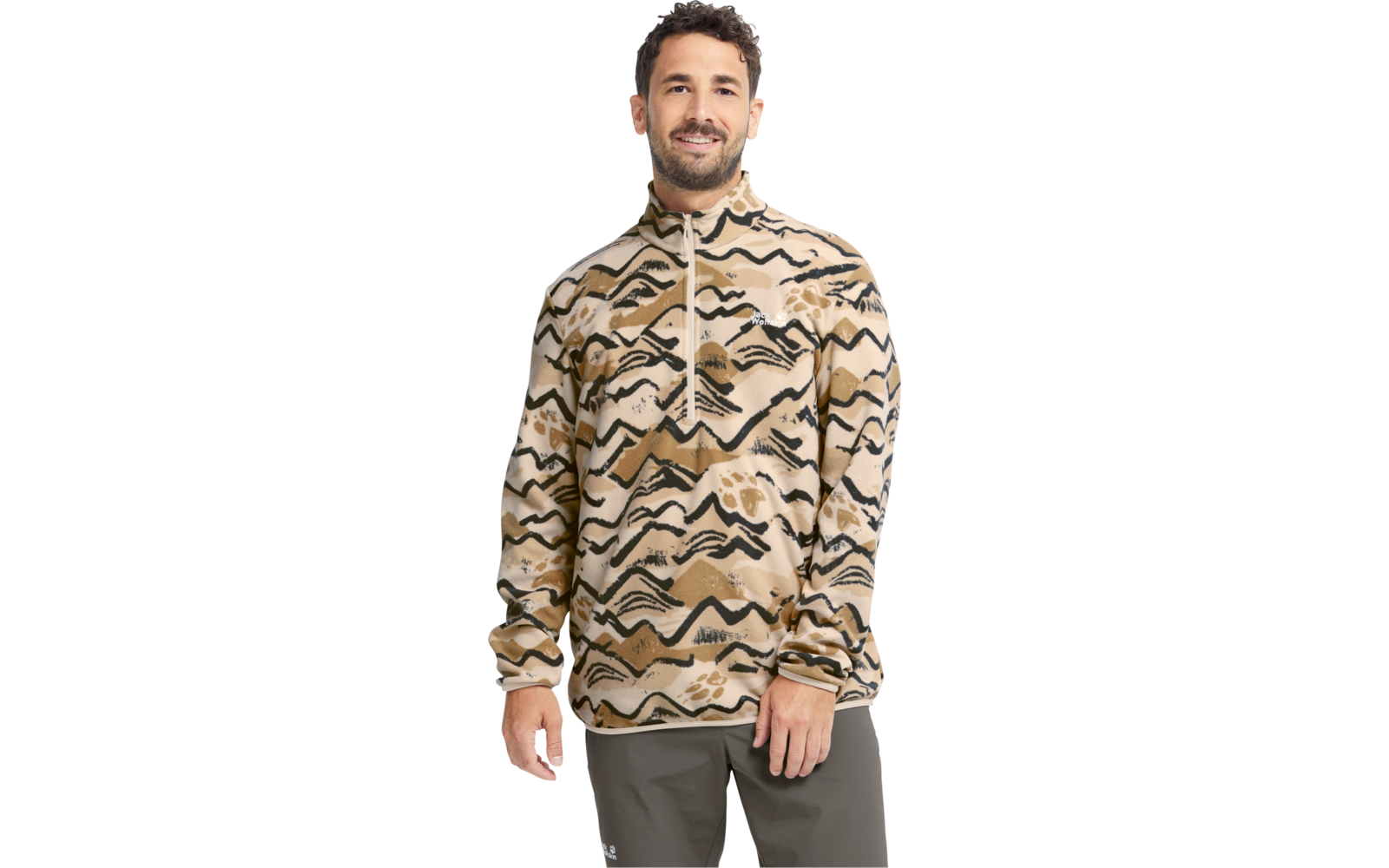 Person steht, trägt beige Zip‑Pullover mit schwarzen, wellenartigen Mustern und dunkelgraue Hose