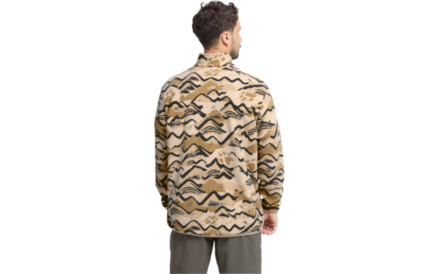 Person von hinten, trägt beige Jacke mit schwarzen geschwungenen und gezackten Mustern, hoher Kragen, lange Ärmel; olivgrüne Hose; kurzes dunkles lockiges Haar