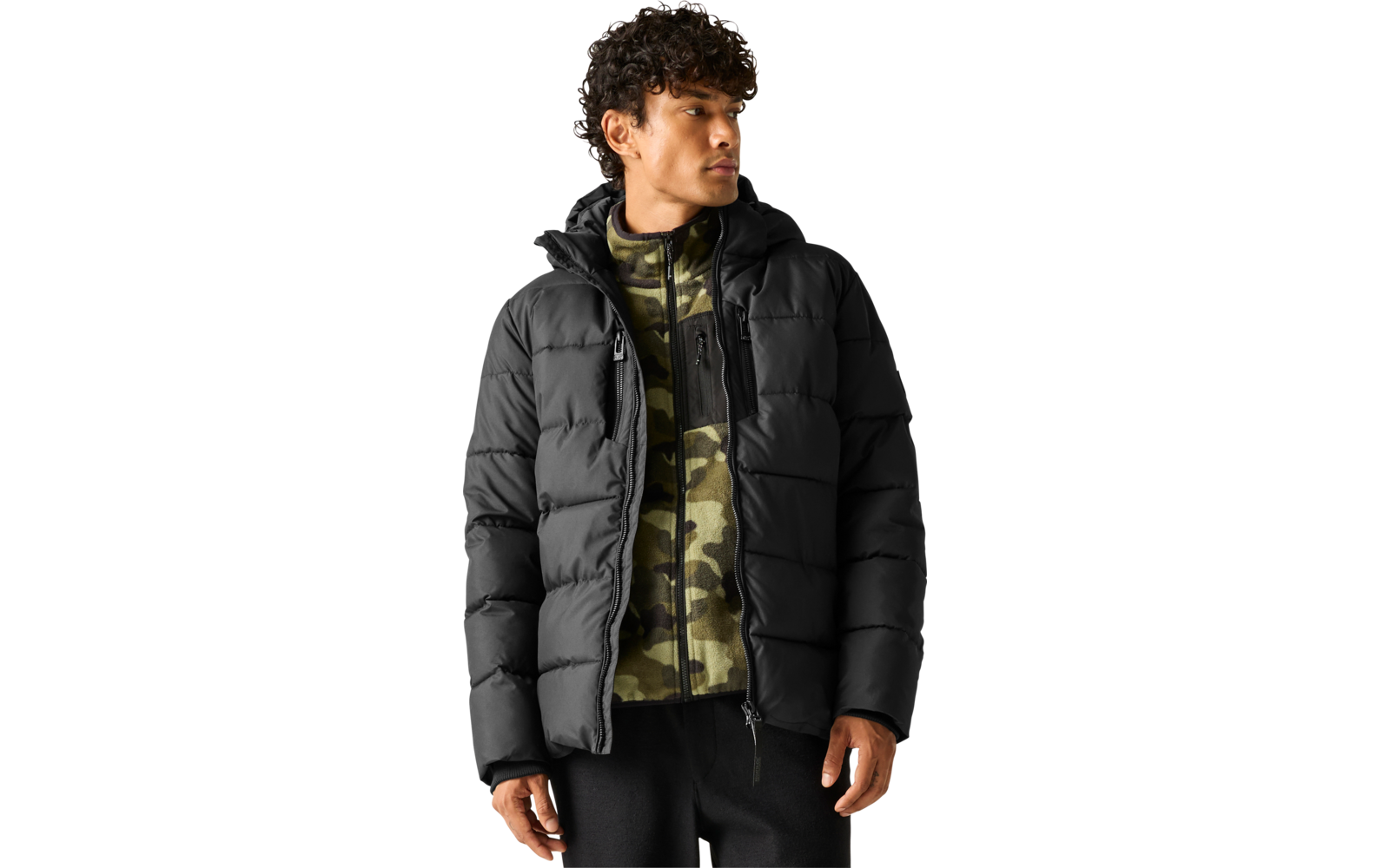 Man met zwarte gewatteerde jas over een groene camouflagefleece met rits, zwarte broek, staand en naar rechts kijkend