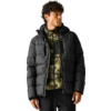 Man met zwarte gewatteerde jas over een groene camouflagefleece met rits, zwarte broek, staand en naar rechts kijkend