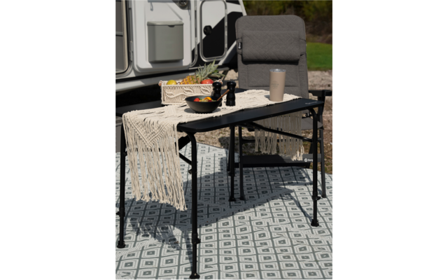 Chaise et table avec nappe et bouteille devant une caravane en plein air