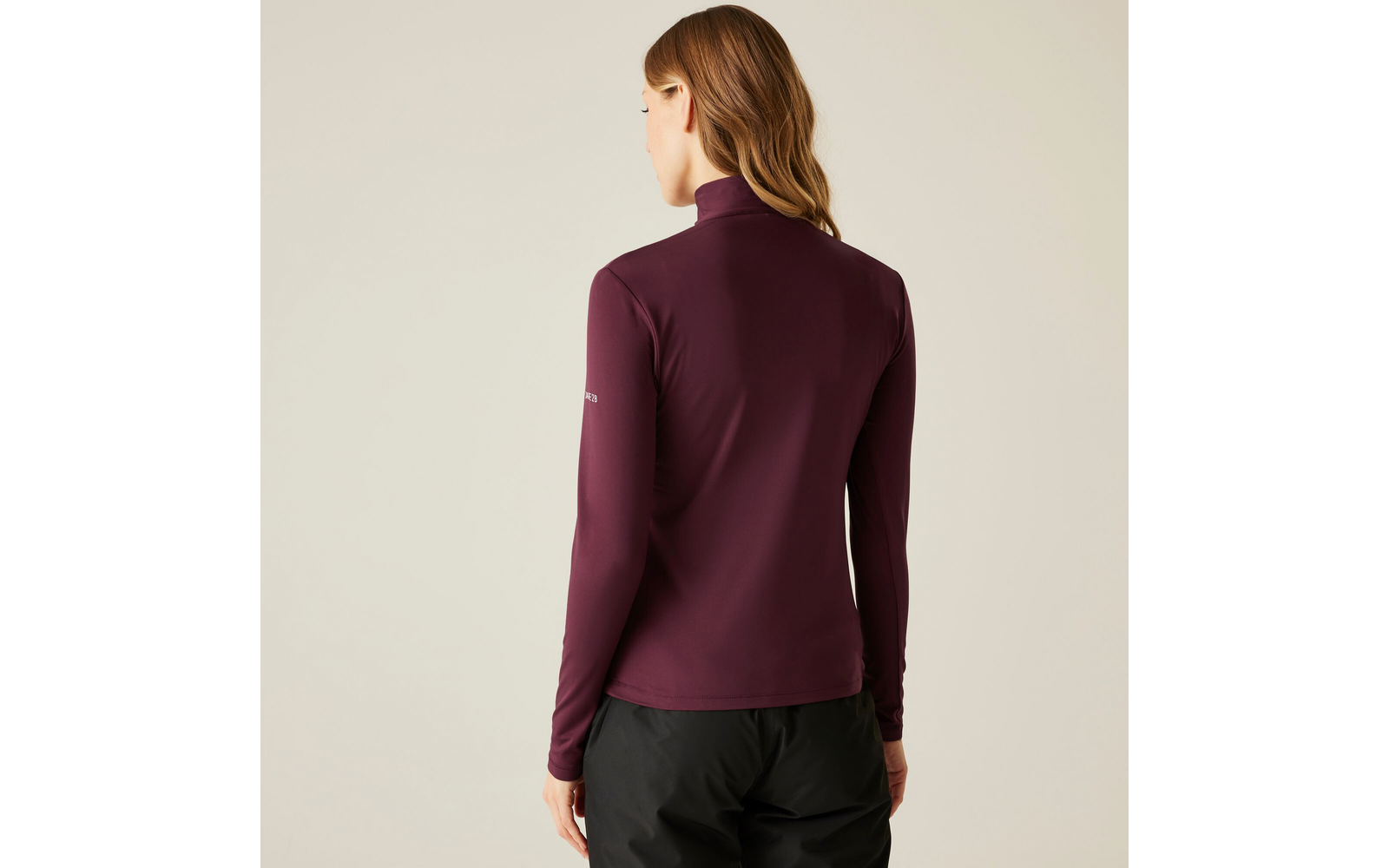 Femme vue de dos portant un haut à manches longues violet foncé et un pantalon noir sur un fond clair
