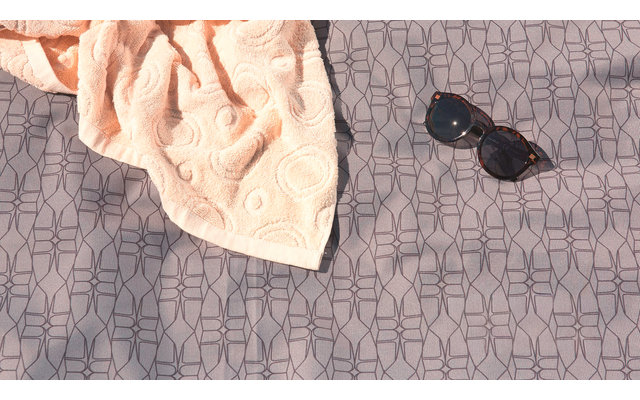 Handtuch und Sonnenbrille auf gemustertem Stoff liegend