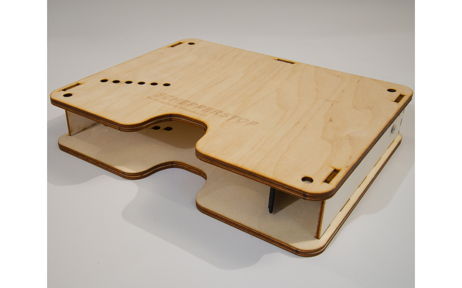 Two stacked light plywood panels with rounded cutouts, rows of small holes, corner slots and visible connecting posts on a white surface