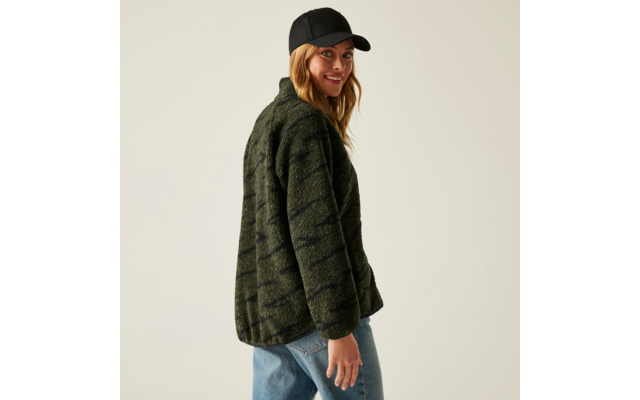 Frau trägt eine grüne Jacke, blaue Jeans und eine schwarze Kappe, schaut lächelnd über die Schulter