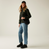 Frau steht vor hellem Hintergrund, trägt schwarze Mütze, schwarze Jacke, blauen Pullover, Jeans und schwarze Schuhe