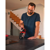 Mann mit Brille und Bart hält roten und schwarzen Handsauger über dunkler Küchenarbeitsplatte, Treppe im Hintergrund