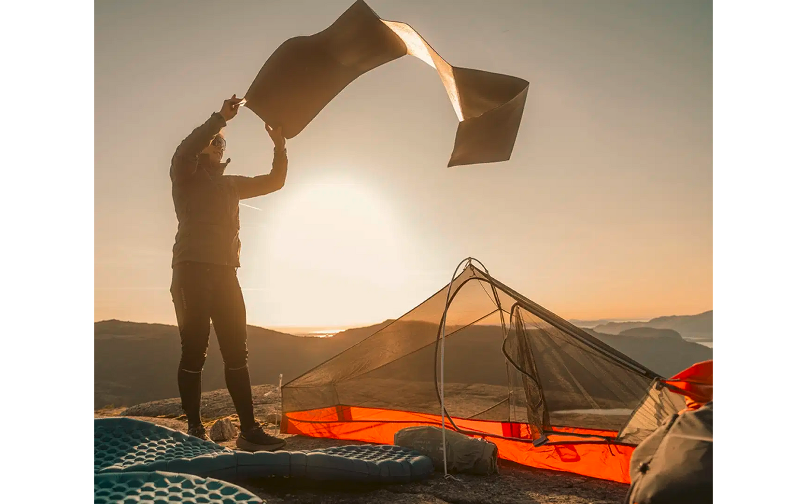 Persoon giet water uit een emmer over een tent bij zonsondergang