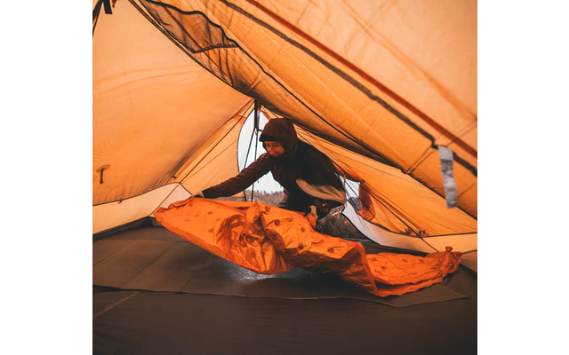 Persoon ligt in een oranje slaapzak in een tent