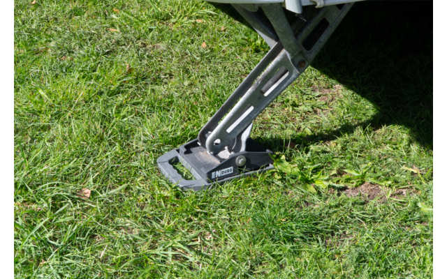 Metallstützbein eines Fahrzeugs auf einer schwarzen Grundplatte auf grünem Gras; Fahrzeugunterboden oben rechts sichtbar