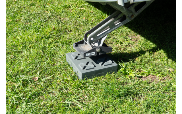 Stützfuß eines Wohnwagens auf einer grauen Kunststoff-Unterlegplatte auf Gras
